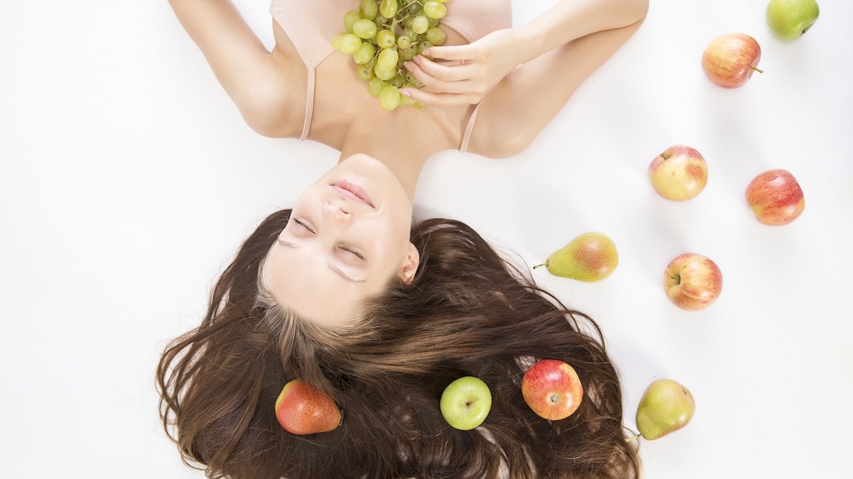 woman lying on white flooring holding grapes beside apple fruits